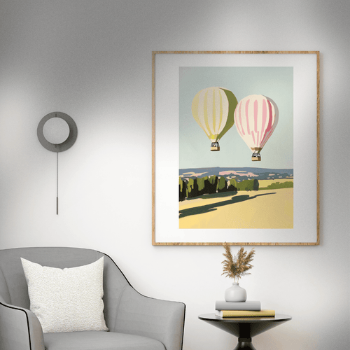 Framed artwork of hot air balloons on a wall above a gray armchair.