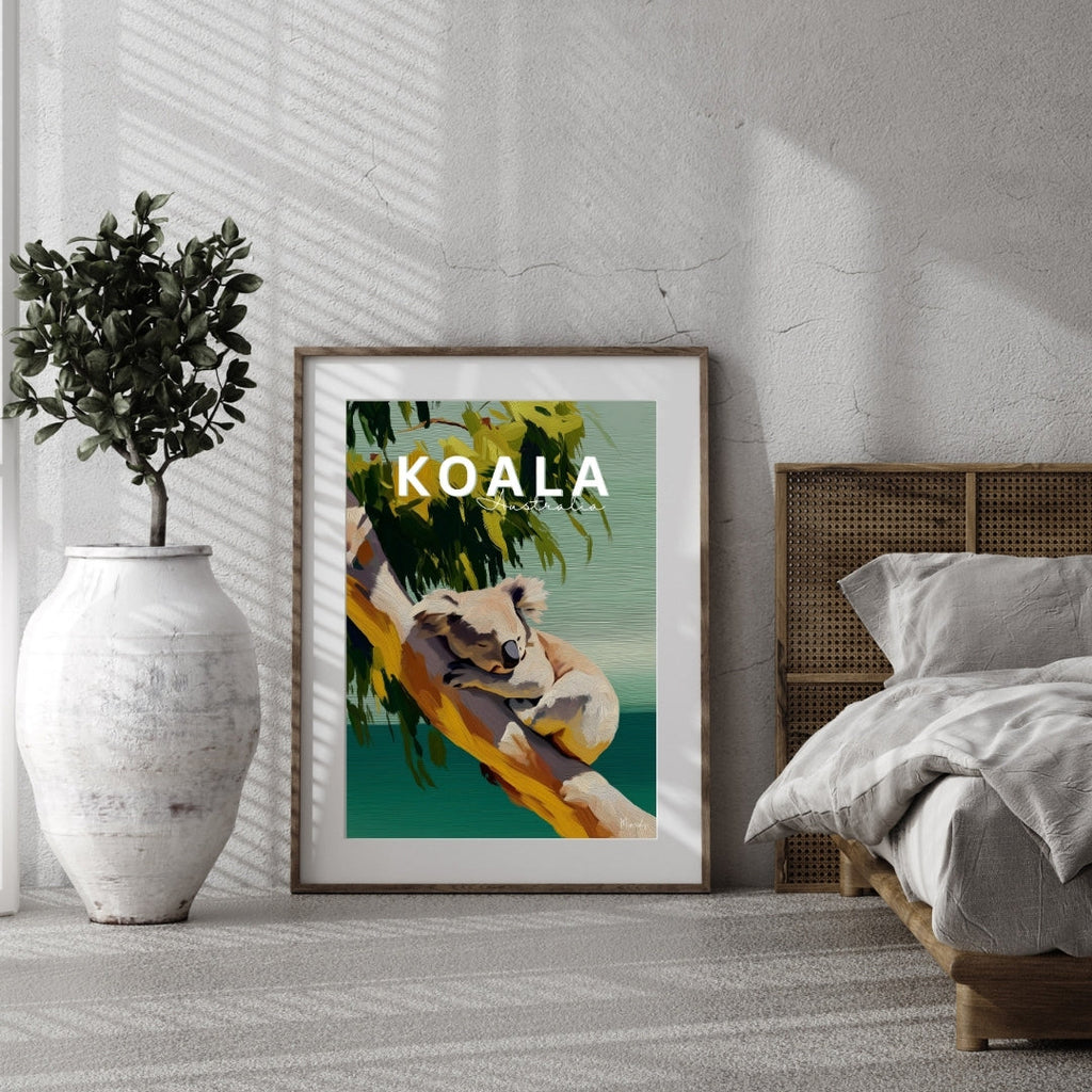 Framed artwork of a koala with the word 'KOALA' displayed in a room with a bed and plant.