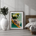 Framed artwork of a koala with the word 'KOALA' displayed in a room with a bed and plant.